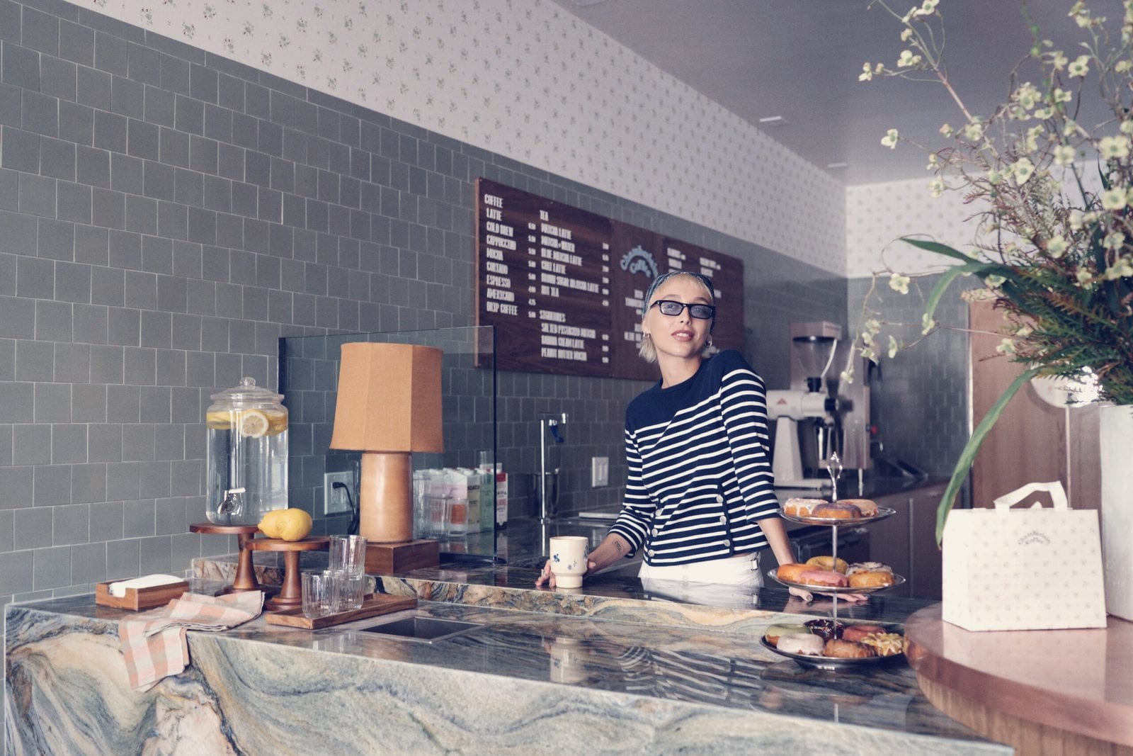 Emma Chamberlain in a striped navy top behind the counter of the Chamberlain Coffee cafe on Abbot Kinney, Venice, May 2026