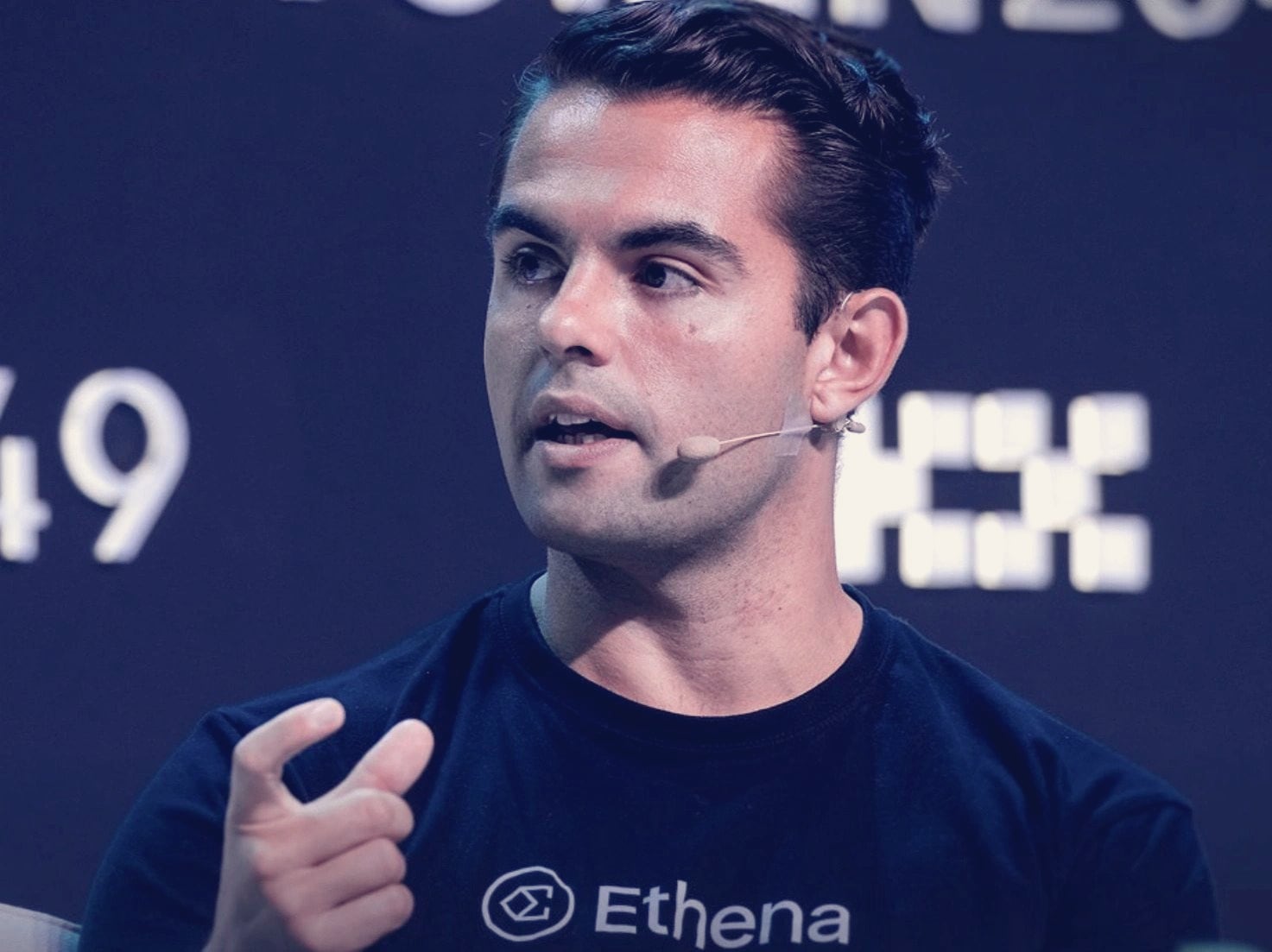 Guy Young, founder of Ethena Labs, speaking on stage at TOKEN2049 in an Ethena T-shirt and headset microphone.