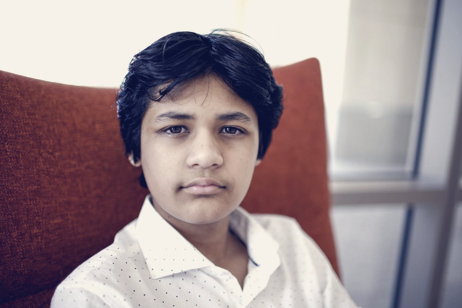 Portrait of Kairan Quazi seated in an orange armchair, looking at the camera