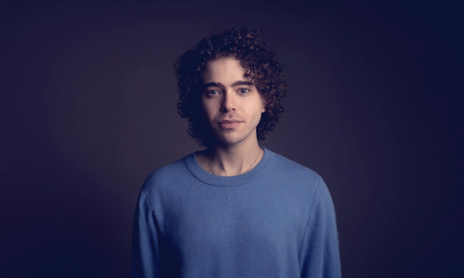 Shayne Coplan, founder and CEO of Polymarket, in a blue sweater against a dark studio backdrop